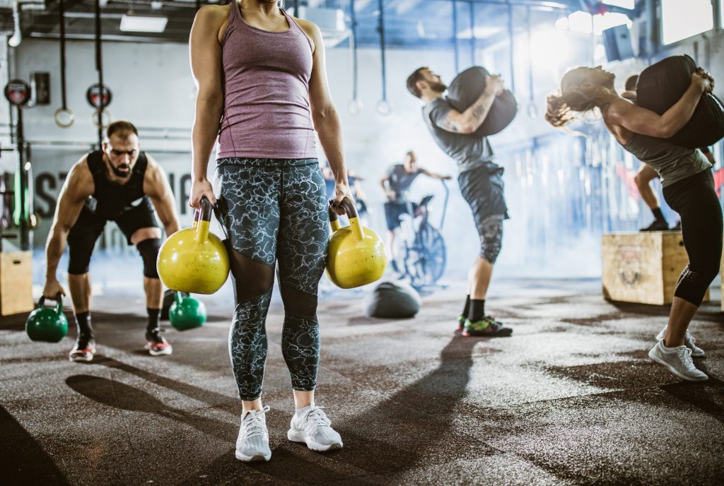 Unrecognisable female athlete exercising with kettle bells during circuit sport training with other people in a health club.